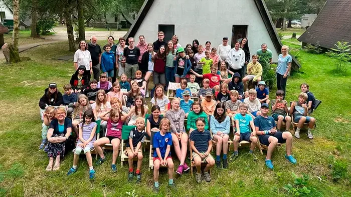 Große Gruppe von Kindern und Erwachsenen, die draußen vor einer Hütte posieren.