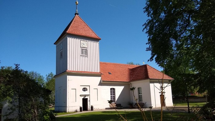 Weißes Kirchengebäude mit rotem Dach und Turm auf grünem Rasen