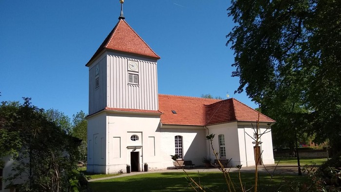 Weißes Kirchengebäude mit rotem Dach und Turm auf grünem Rasen