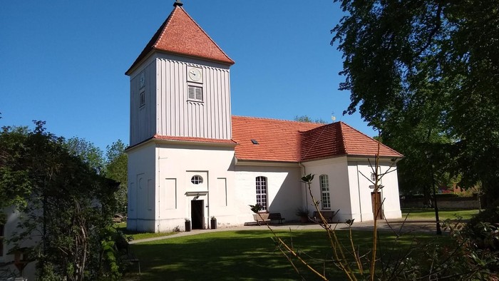 Weißes Kirchengebäude mit rotem Dach und Turm auf grünem Rasen