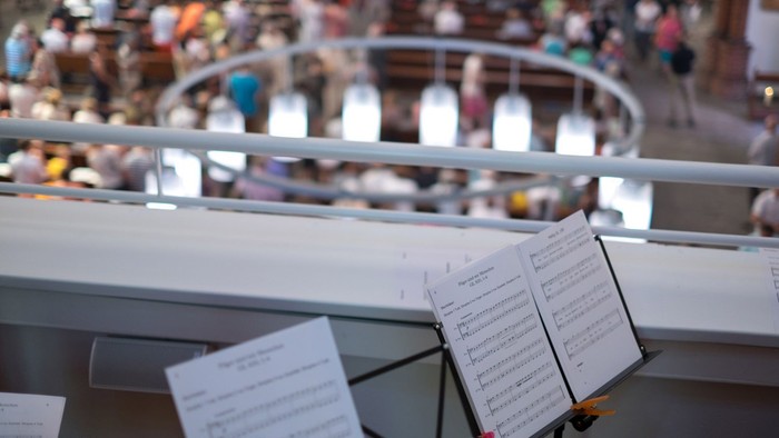 Notenständer mit Notenblättern auf Bühne, Publikum im Hintergrund