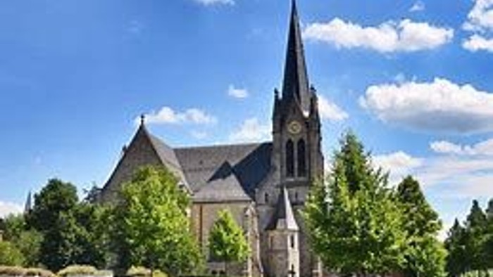 Große Kirche mit hohem Turmspitz, umgeben von grünen Bäumen und Gras.