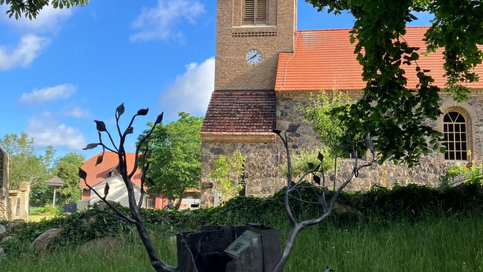 Kirchturm mit Uhr, davor Skulptur im Park