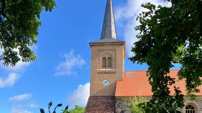 Kirchturm mit Uhr, davor Skulptur im Park