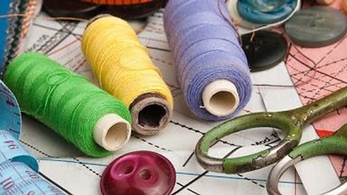 Colorful spools of thread, scissors, and sewing supplies arranged on a patterned background.