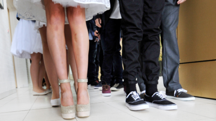 En brud og to mænd står sammen, brudens sko er høje og glitrende, mændenes sko er simple og mørke.