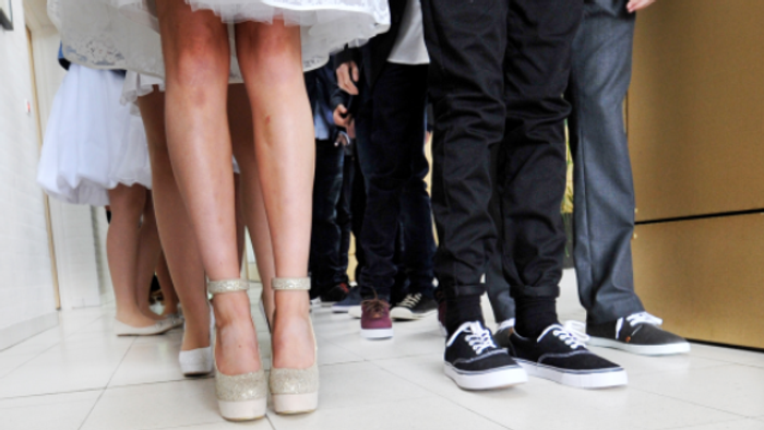 En brud og to mænd står sammen, brudens sko er høje og glitrende, mændenes sko er simple og mørke.