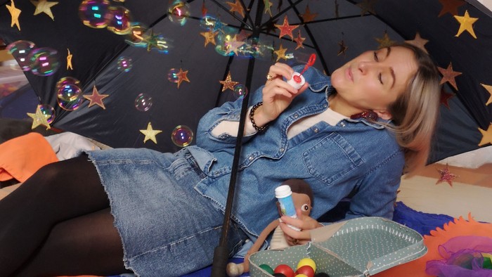 Et barn ligger under en regnbuet med stjerner og spiller med legetøj.