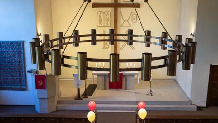 Ein ruhiger Kirchengang, gesäumt von Luftballons, der zu einem geschmückten Altar- und Kanzelbereich führt.