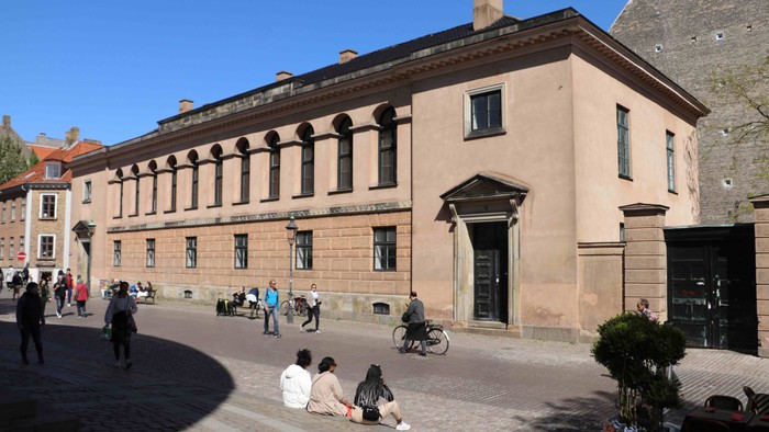 En stor, lilla bygning med kolonner og en gruppe mennesker udenfor.