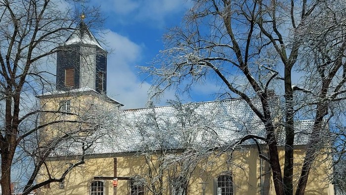 Eingeschneite Kirche mit hohem Turm und kahlen Bäumen im Winter