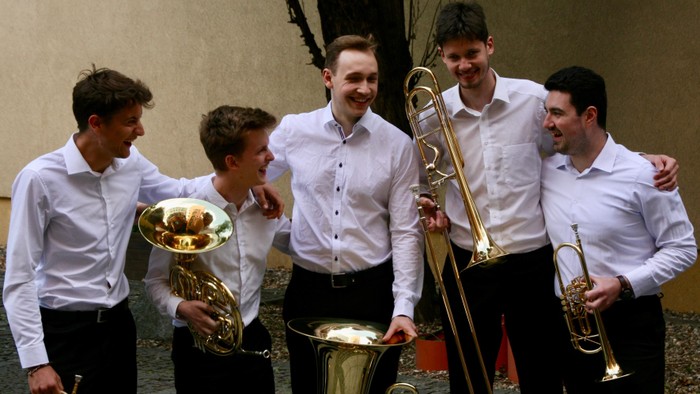 Eine Gruppe von fünf Musiker:innen, die gemeinsam im Freien posieren und verschiedene Blechblasinstrumente halten.