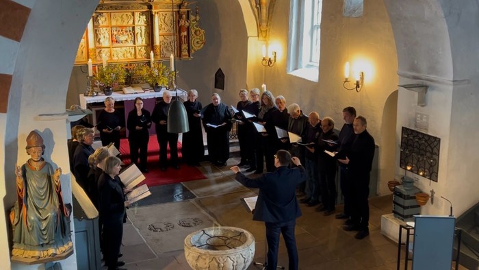 Ein Chor singt in einer Kirche, umgeben von alten Gemälden und Kerzenlicht.