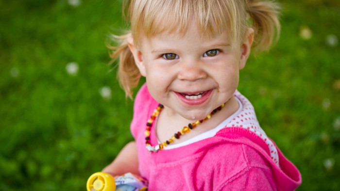 Ein kleines Mädchen mit Zöpfen lacht in einem grünen Garten und hält ein Spielzeug.