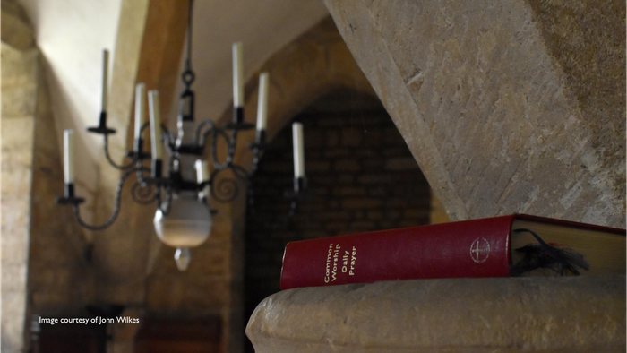 A red book rests on a stone ledge beneath a chandelier in a rustic room.