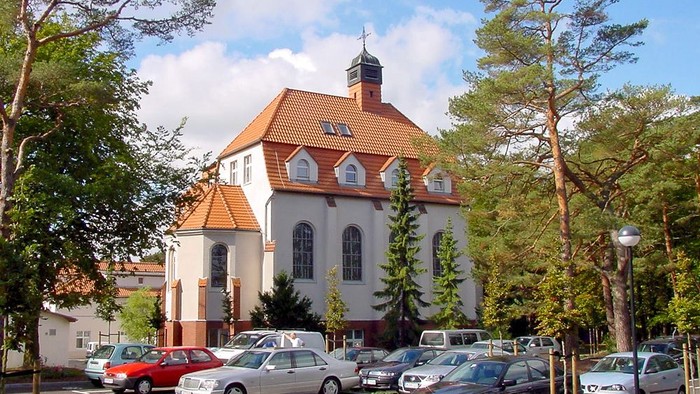 Parkplatz vor weißem Gebäude mit rotem Dach und Turm.