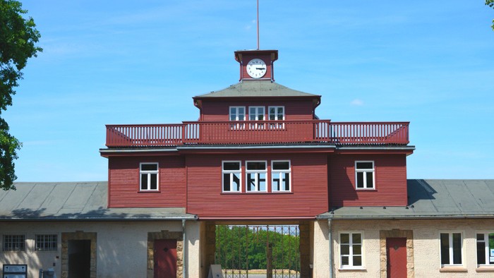 Das Bild zeigt ein rotes Gebäude mit Uhr und Balkon unter blauem Himmel.