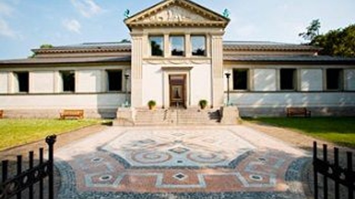 Et stort, klassisk hus med indgangsporten og en indgrovet bane foran