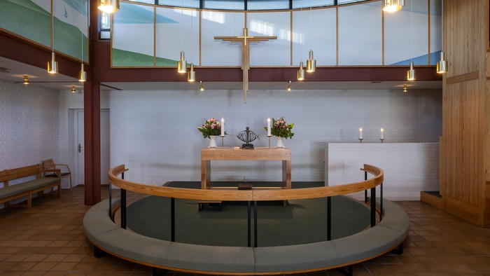 En moderne kirkeinterior med central alter og hængende lygter