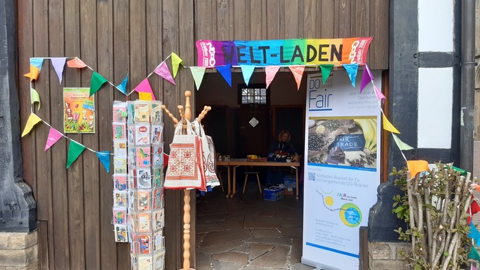 Bunte Flaggen und Banner schmücken den Eingang zu einem Laden mit verschiedenen Artikeln und einer Infotafel.