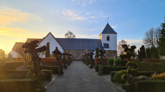 En lille kirke med tårn og gravsteder ved solnedgang