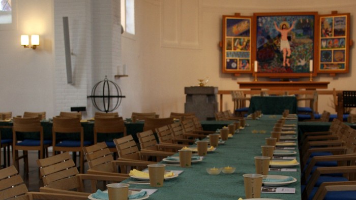 En kirkesal opsat med engangs tallerkener, kopper og bestik til et fællesmåltid eller arrangement.