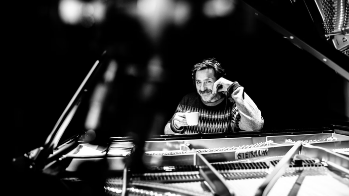 En person spiller på et flygel med en kop kaffe, og virker fokuseret og engageret i en svagt oplyst omgivelse.