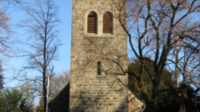 Alter Kirchturm mit Uhr und buntem Glasfenster, umgeben von Bäumen