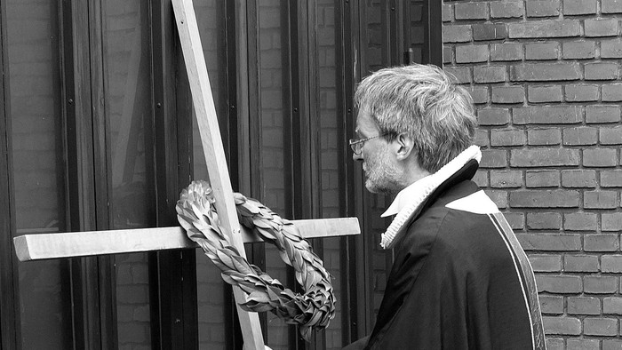 En kvinde i mørkt kapel og hvid kjole holder en stor blomstertop.