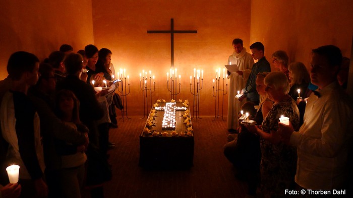 En gruppe af mennesker holder lysede lygter i en kirke.