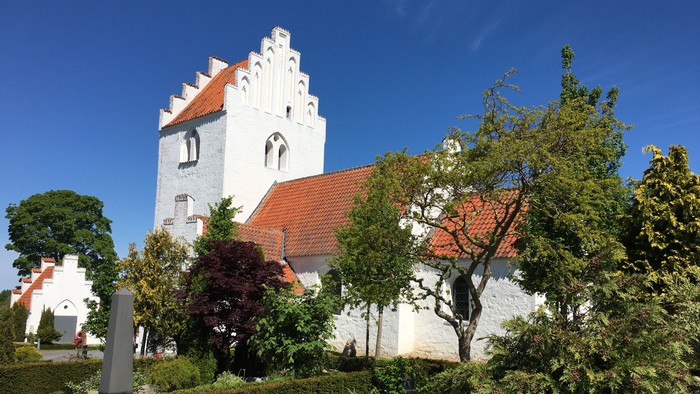 Hvid kirke med røde tag og træer foran