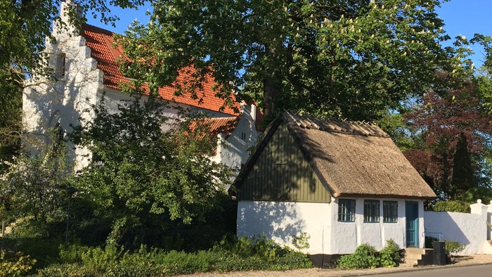 Klokkerhuset med træer og kirken i baggrunden