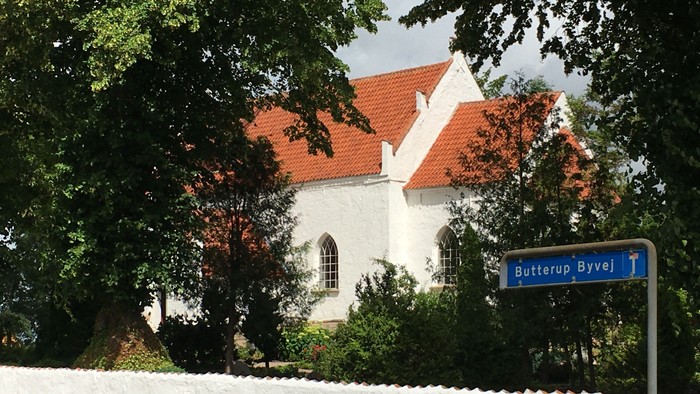 Hvid kirke med røde tagtegn og skilt med 'Butterup Byvej'
