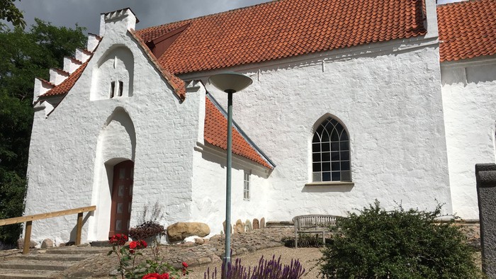 Hvid kirke med rødt tag og røde blomster i forgrunden