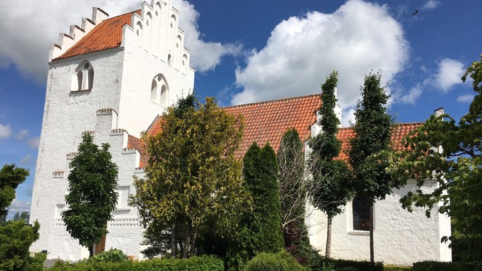 Et hvidt kloster med røde tag og en klokketårn omgivet af grønne planter og træer