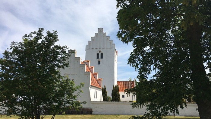 Et hvidt tårn med røde tag i træernes skygge
