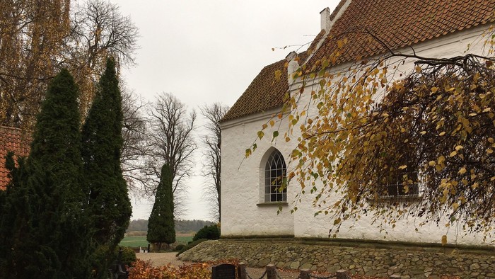 En gammel hvidkalket kirke med rødt tag og efterårsblade