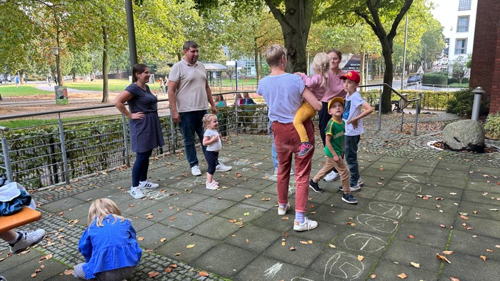 En gruppe børn og voksne spiller på en plæne med tegnede hoppebænke.