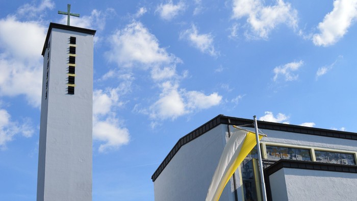 Moderne Kirche mit hohem Glockenturm und geschwungenem Eingangsüberdach unter einem strahlend blauen Himmel.