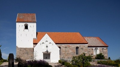 En hvid kirke med røde tag og tårn foran en klar blå himmel