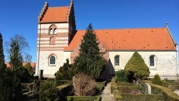 En gammel kirke med røde tag og en have med træer og buske