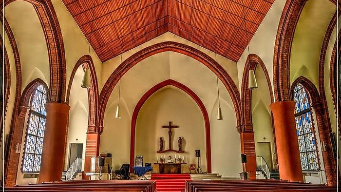 Elegante Kircheninnenraum mit hölzernen Kirchenbänken, gewölbten Decken, Buntglasfenstern und einem zentralen Kruzifix-Altar.
