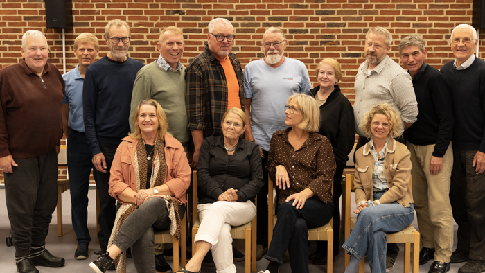 En gruppe af mennesker sidder og står sammen i en hal, alle smiler til kameraet