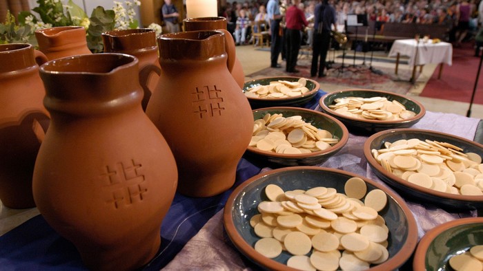 Auf dem Tisch stehen Töpfergefäße und Schalen mit Brezeln, im Hintergrund Menschen.