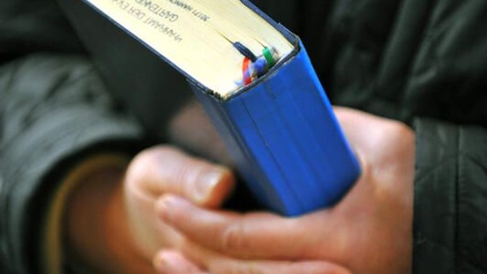 Person mit einem blauen Ordner mit gelbem Rücken, gefüllt mit Papieren oder Notizen.