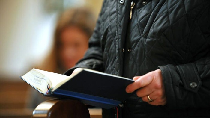Person in einer Steppjacke, die ein offenes Buch liest, möglicherweise ein Gesang- oder Gebetbuch.