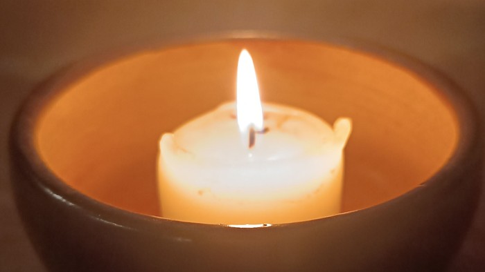 Eine brennende Kerze in einer dunklen, warmtönigen Schale, die sanftes, mildes Licht wirft.