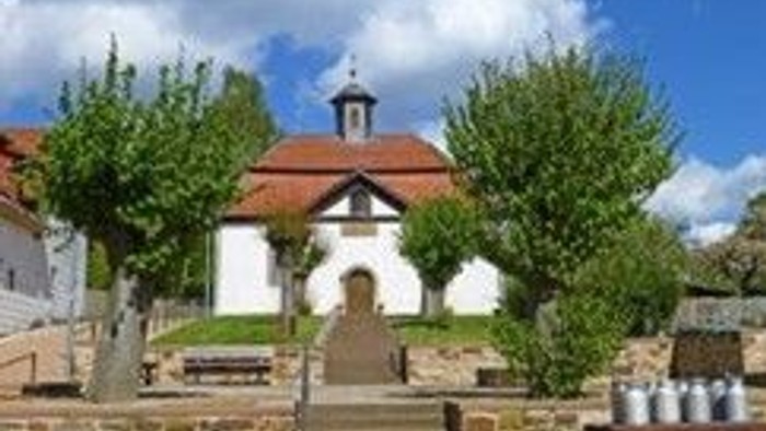 Idyllische Kirche mit Treppen, die zum Eingang führen, umgeben von Bäumen und einer ruhigen Dorfkulisse.