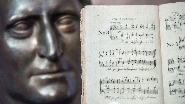 Eine Bronzebüste, teilweise verdeckt von einem aufgeschlagenen Blatt klassischer Noten mit musikalischen Noten.