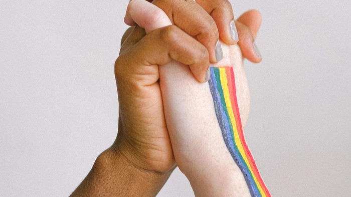 Zwei Hände halten sich fest, eine mit bunter Armbinde